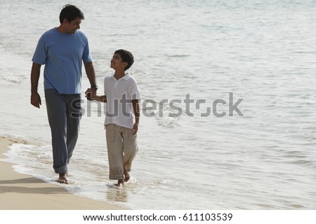 Father and son holding hands and walking on beach