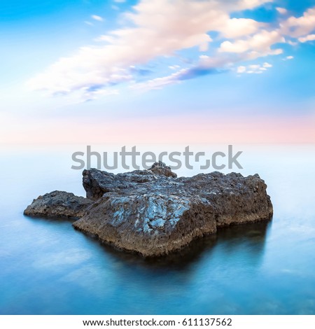 A rock in a blue ocean under cloudy sky on horizon. Long exposure photography. 