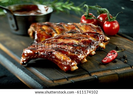 Spicy hot grilled spare ribs from a summer BBQ served with a hot chili pepper and fresh tomatoes on an old vintage wooden cutting board Royalty-Free Stock Photo #611174102