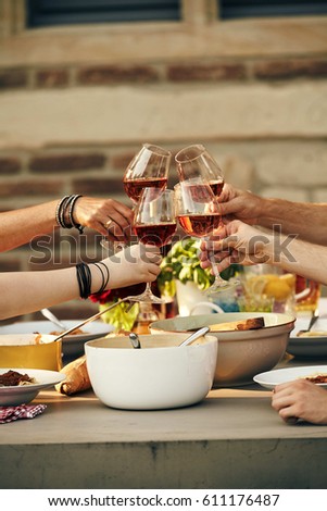 Young friends clinking wineglasses in a toast as they enjoy a meal of fresh spring salad and Italian pasta outdoors in the sunshine
