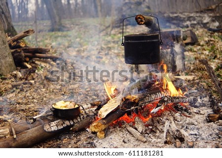 Tourist kettle on camp fire with tent on background. hand with stick about fire.