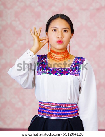 Young woman wearing traditional andean dress, facing camera doing sign language word for woman