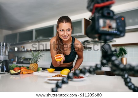 Young woman recording food based video content on camera. Woman showing a cut orange facing the camera.