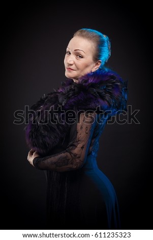 Portrait of a beautiful mature woman in a theatrical costume with boa posing on a black background