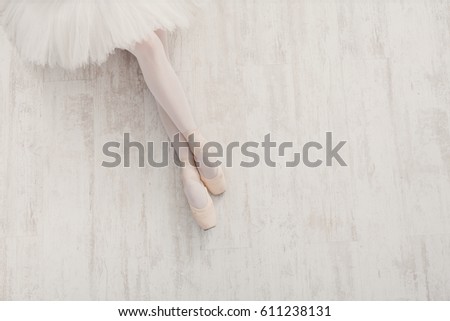 Ballet background. Closeup of young ballerina legs in pointe shoes on white wooden floor, top view from above with copy space. Ballet practice. Beautiful slim graceful feet of dancer.