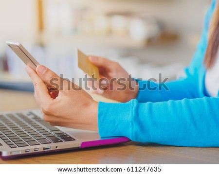 Pretty Young womans hands holding a credit card and using smartphone and laptop computer for online shopping. Online payment. Female working on smart phone laptop in a cafe.