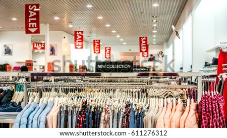 small black plate above new shirts and pants in different colors what hung on hangers in big shop. collection with plate in a clothing store with a sign NEW COLLECTION