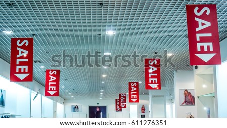 two rows of red vertical sale posters with white letters hang from grid ceiling in big shop in sale season. sale poster board at fashion clothes shopfront