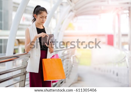 Beautiful woman looking in open wallet with shocked expression while holding color shopping bags Royalty-Free Stock Photo #611305406