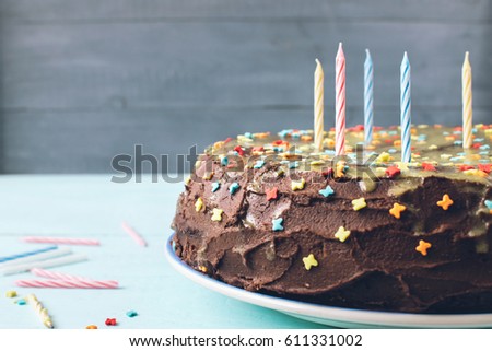 Chocolate cake with chocolate icing for birthday with festive candles. Blue wooden background, copy space. Selective focus, close-up