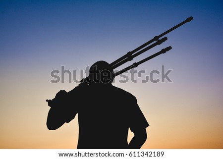 male photographer silhouette with  holding tripod