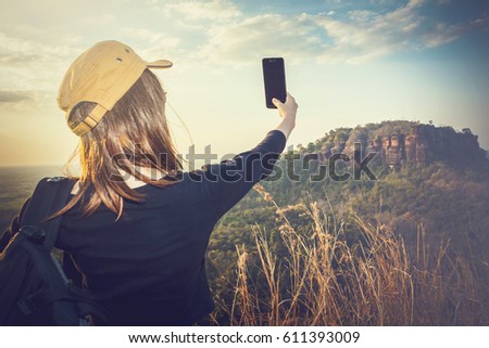 Female tourists are taking photos with their mobile phones over mountain background.