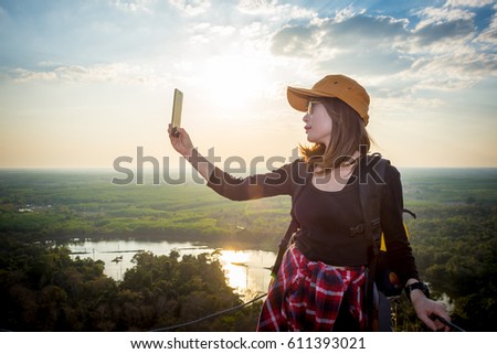 Female tourists are taking photos with their mobile phones over sunset background.