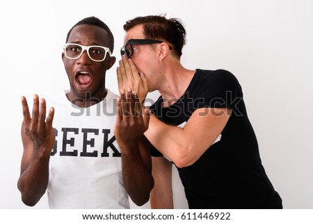 Studio shot of young black African Geek man listening while European Nerd man is whispering and telling something