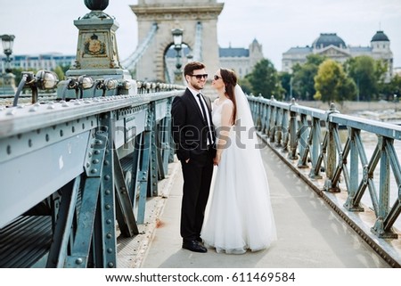 Gorgeous bride with curly hair and bridegroom standing close to each other on bridge at old city background, wedding photo, Budapest city.