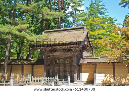 Viewed from a public street, a weathered wooden gate with a thatched roof stands at the entrance to a Buddhist temple park in Koyasan, Japan, a UNESCO World Heritage Site.