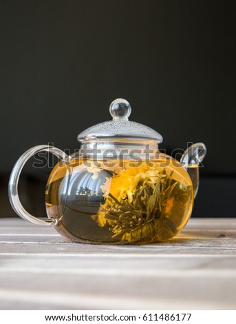 a glass tea pot with Flower Chinese tea on light wooden table in front of dark background. vertical