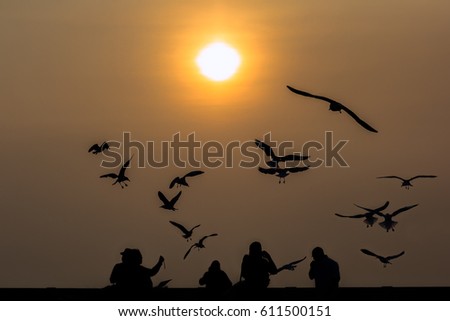 Silhouette of Seagulls fly in the sky and family enjoying a beautiful sunset at Bang Pu,Thailand