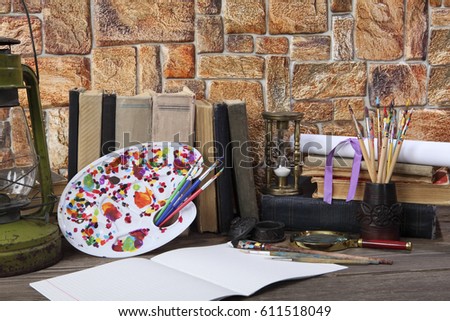 Old books, an easel, brushes, an hourglass, a magnifying glass, a kerosene lamp on a table. Retro stylized photo