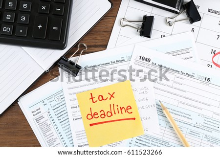 Paper sheet with text TAX DEADLINE and individual tax return form on table