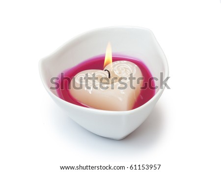 Beautiful burning candle in the shape of the heart, in a dish on a white background. / Burning candle