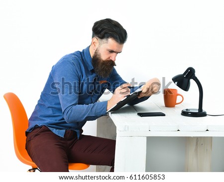 Bearded man, long beard. Brutal caucasian unshaven serious hipster with moustache writing to notepad, sitting at white vintage wooden table with black lamp on it, isolated on white background