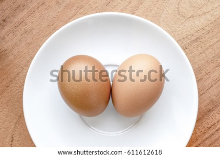 Two chicken eggs in white plate  on wooden on wooden background , top view and selective focus with copy space