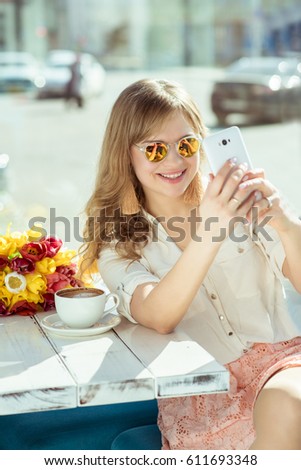 Smiling girl makes a selfie sitting on the terrace of cafe