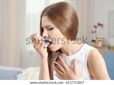 Young woman using asthma inhaler at home Royalty-Free Stock Photo #611711867