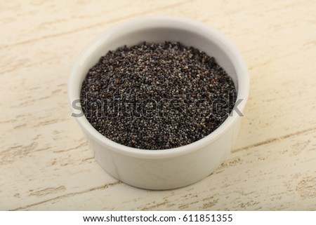 Poppy seeds in the bowl over wooden background