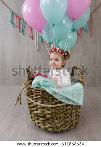 Little girl sitting in a basket with big air balls on a gray background