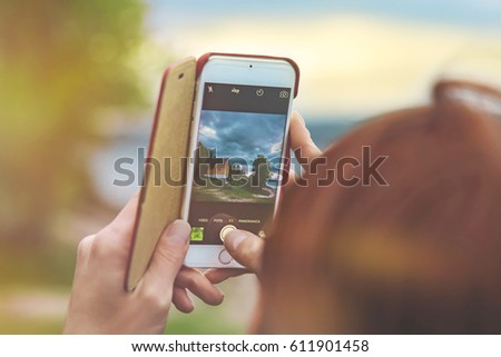 Female hands hold the smart phone while shooting a landscape in Norway at sunset light