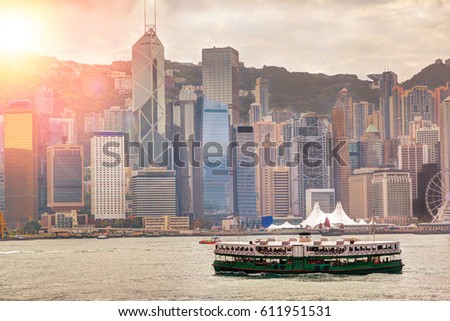 Morning sunrise with deliberate lens flare over Hong Kong skyline and ferry crossing Victoria Harbor. HDR rendering.