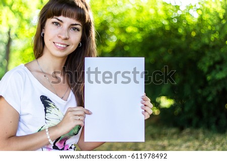 Banner for your message: Lovely teen-girl holding clean white sheet paper, in the park.