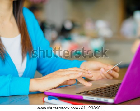 Pretty Young womans hands holding a credit card and using laptop computer for online shopping. Online payment. Female working on laptop in a cafe.