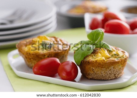 Two mini quiches served on white plate. Delicious vegetarian vegetable pies sprinkled with cut basil and set on green and white clad table with cherry tomatoes