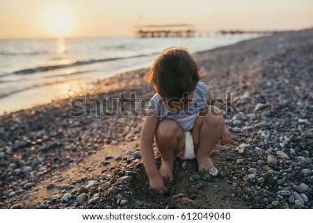 Beautiful cute girl toddler play at the sea beach sunset background. Happy family summer vacation. Travel. Caucasian happy baby sit play game activity at ocean sunset Childhood lifestyle. Silhouette.