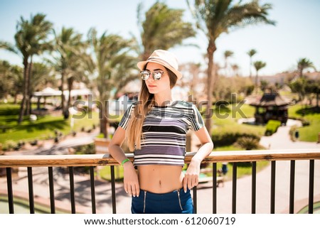 Relaxed happy smile young woman in hat and sunglasses on terrace of hotel on palms background. Summer vocation