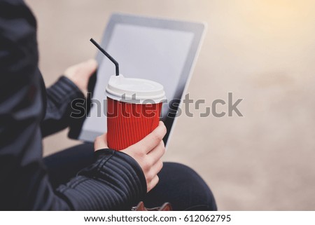 Cup of coffee in hand and tablet on background.
