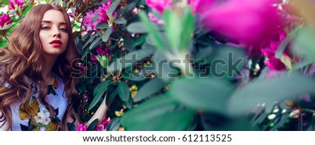 Beautiful young girl with lush hair in paradise garden. A luxurious dress, make-up. Pink flowers, large green leaves, Banner, advertising, fashion, beauty, spa. Bright, rich picture.
