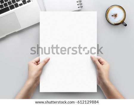 Hand holding paper a4 on white office desk table top view with copy space