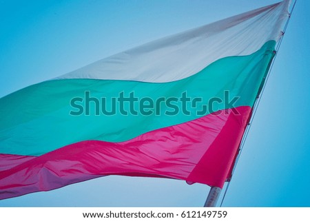 Tree-colored Bulgarian flag waving on the clear blue sky background.