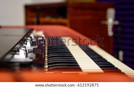 A close up view of the keys and draw bars of a vintage tone wheel organ and rotating speaker blurred in the background. 
