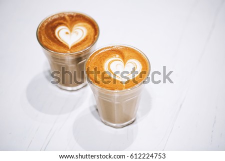 Two glass cups of cappuccino with latte art on white wooden table.