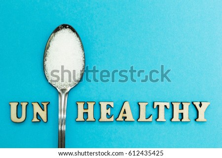 The word "un healthy", a spoon with sugar on a blue background, concept.