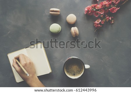 Girl hand, notebook,  coffee, macarons and flowers on cement background
