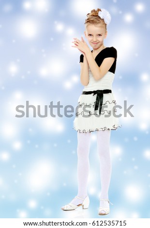 Beautiful little blonde girl dressed in a white short dress with black sleeves and a black belt.Girl poses for the camera.Blue Christmas festive background with white snowflakes.