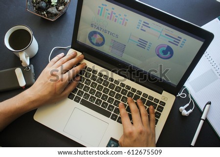 Young businessman working with data and making business plan at laptop hands closeup near smart phone, coffee and notepad, young handsome man working in office workspace, top view