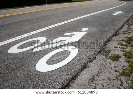 Bike Lane Symbol with Arrow at an Angle Next to the Road with Yellow Lines, Dirt and Grass on Either Side, in a Sunny Afternoon at Trade Winds Park, Pompano Beach, Florida
