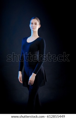 Portrait of a young ballerina girl dancer shows dance elements on a black background in a blue stage light